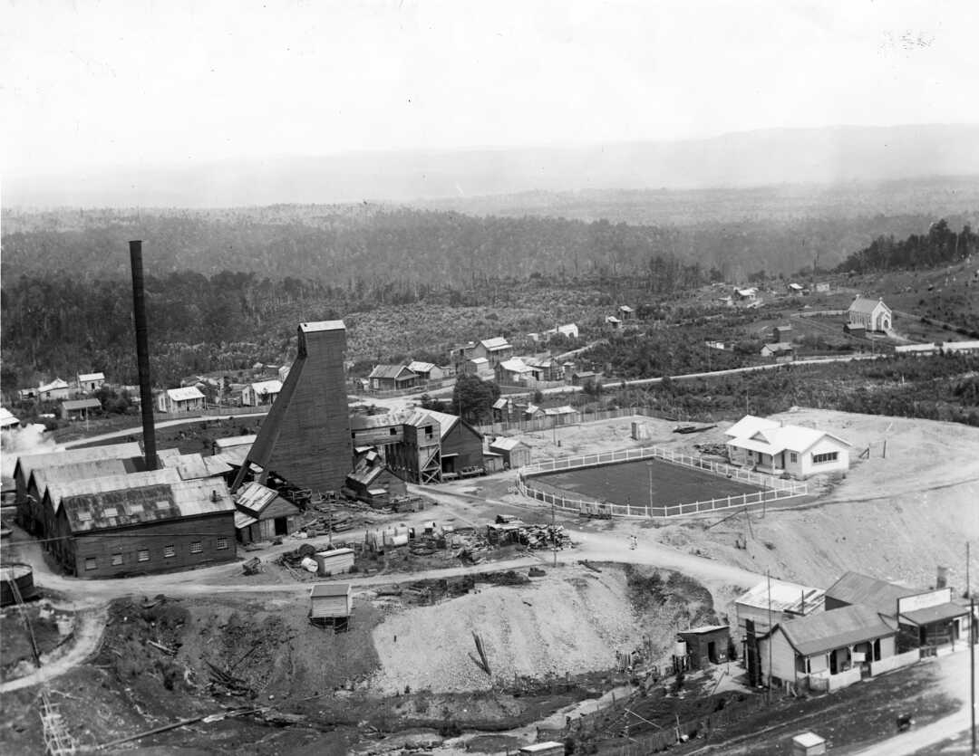 Waiuta, West Coast. c.1930s Township and the south shaft. The bowling club and green can be seen forground right, and on the left can be seen the tower and buildings associated with the Blackwater Mine's south shaft. Ref: PAColl-4796-15
